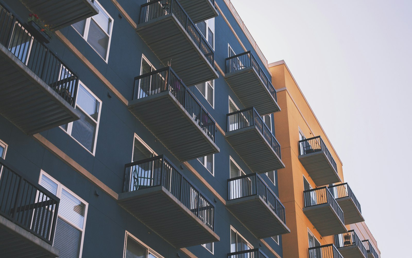 Exterior corner of a multi-storey balcony building against an open pale sky